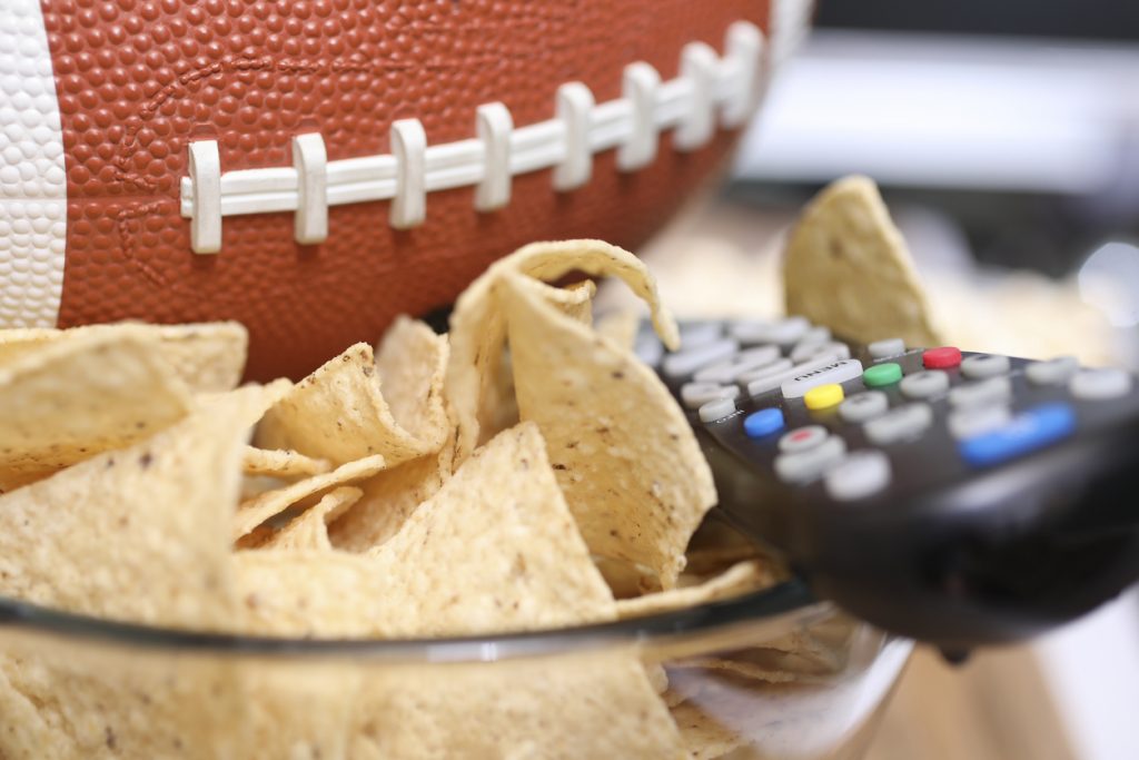 footbal next to a snack bowl and remote control