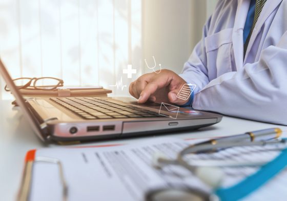 doctor using laptop with medical icons floating above keyboard